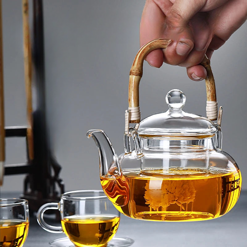 a person holding a glass tea pot with a wooden handle