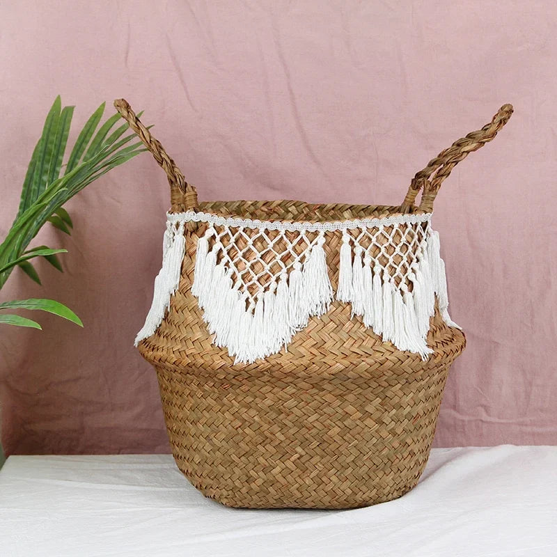 a woven basket with tassels on a table next to a potted plant