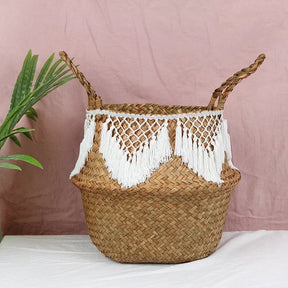 a woven basket with tassels on a table next to a potted plant